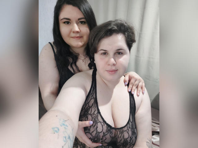 BeckyAndEllen, vêtue de lingerie en dentelle noire, montrant ses seins, se tient derrière Ellen, qui a les cheveux courts et bruns, et qui touche ses seins, toutes deux souriant, la main de BeckyAndEllen sur la poitrine d'Ellen..