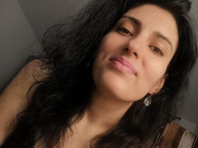 AddictedToUTS has long black hair, pink lips, and is smiling slightly with her eyes half-closed. She's wearing a small, shiny earring on her left ear.