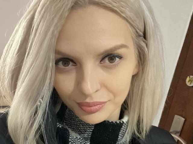 DouceAmelia tiene cabello rubio, piel clara, ojos marrones y labios rosados. Lleva un pañuelo a cuadros negros y blancos, y mira directamente a la cámara con una ligera sonrisa..