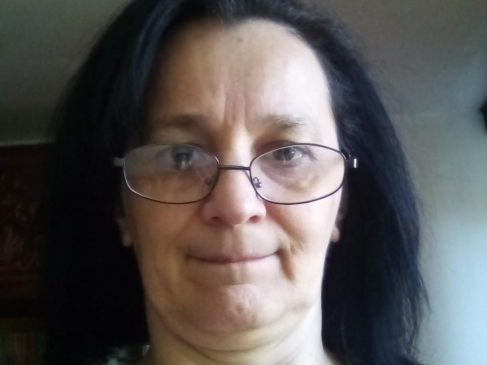 SorayaStar hat schwarzes Haar, eine Brille und ein leichtes Lächeln, wobei man Falten auf ihrem Gesicht sieht. Ihre helle Haut und ihre kleine Nase sind auffällig. Sie wirkt entspannt..