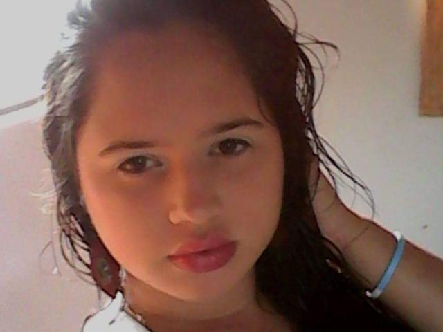 ShalomonTalban has wet black hair, brown eyes, and pink lips. She's wearing a white top with a blue strap, looking at the camera with a slight pout.