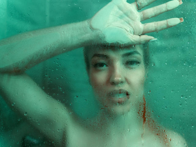 MaisyWarner sous l'eau, main sur le verre, regardant vers le haut, peau mouillée, marques rouges sur la poitrine, eau verdâtre, gouttes d'eau, bouche légèrement ouverte, mamelons visibles, lumière douce, légèrement flou..