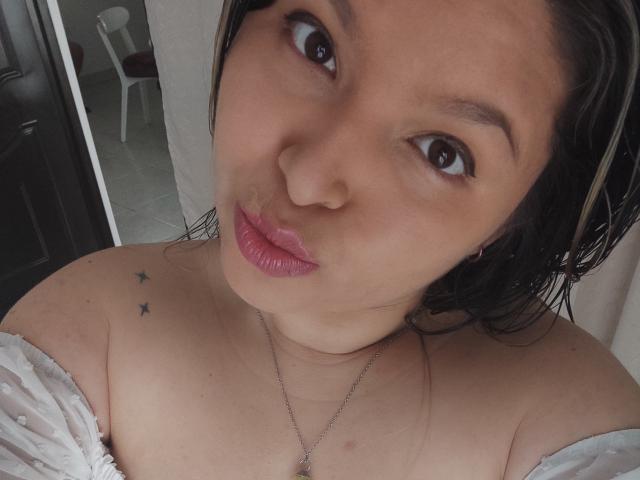Myalewwis has a cute face, brown eyes, and pouty pink lips. She's wearing a white off-shoulder top, showing small star tattoos on her left shoulder.
