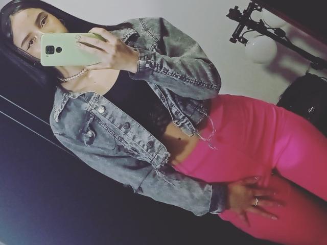 Yukio mit langen, schwarzen Haaren, die eine Jeansjacke, ein schwarzes Oberteil und eine rosa Hose trägt, hält ein Telefon, zeigt ihr Gesäß, in einem Spiegel-Selfie..
