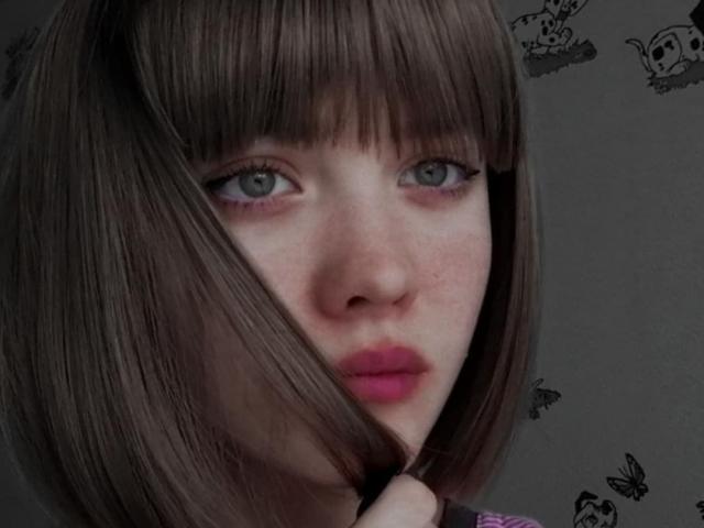 KiraLisa's face, with brown bob and bangs, green eyes, pink lips, holding her hair, showing freckles, and wearing subtle makeup, in a soft-focus, realistic photograph.
