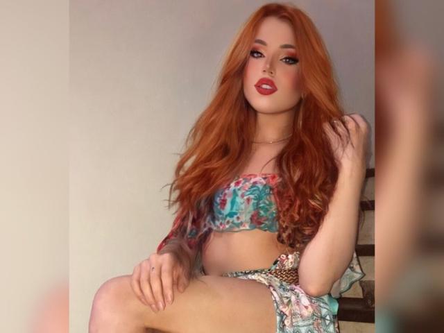 Sophie, eine Fantasy-Figur mit langen roten Haaren, trägt einen farbenfrohen BH mit Blumenmuster und passende Shorts. Sie sitzt mit einer Hand in ihrem Haar und präsentiert ihre Brüste und ihren Hintern..