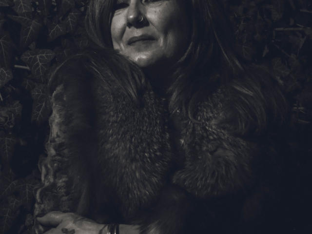 Freya Davidson, met een neusring, draagt een behaarde jas, heeft donker haar, glimlacht lichtjes, met gekruiste armen, op een donkere, sfeervolle zwart-witfoto..