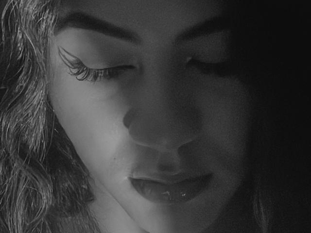 Le visage de KataMillerr, monochrome, les yeux fermés, une ombre sombre sous le nez, des lèvres brillantes, des cheveux ondulés, de longs cils, un maquillage subtil, une lumière douce, une peau lisse, une expression douce, des lèvres légèrement entrouvertes..