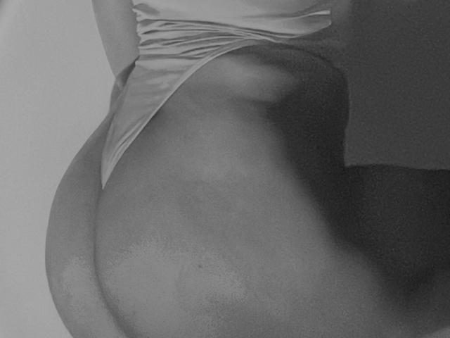 Les fesses de KataMillerr sont mises en valeur par des sous-vêtements ajustés, révélant ses courbes douces et une partie de sa cuisse. En noir et blanc, légèrement flou, mettant en évidence sa peau douce et ses ombres délicates..