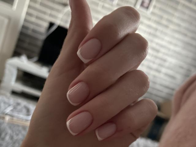 RozalinaPleasure's Hand mit zartrosa Nagellack und weißen Spitzen, leicht gekrümmte Finger, im Fokus, zeigt glatte Haut und ordentlich gepflegte Nägel..