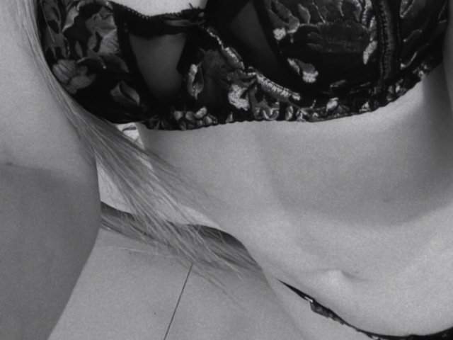 ScarletBeautty's tits in a black floral lace bra, with a slight view of her flat, toned belly and blonde hair falling to the side. Black and white photo.