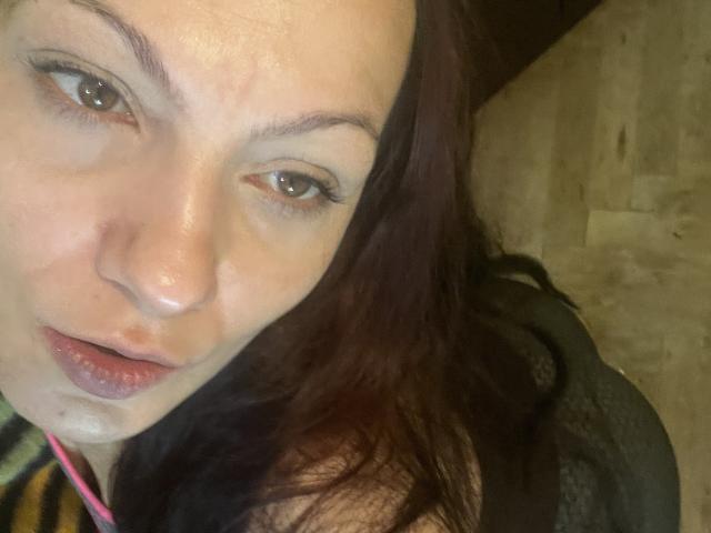 Het gezicht van AamyBeatrice, met een lichtelijk bezwete, bleke huid, bruine ogen, donkerrood haar en roze lippen, met een klein wit vlekje op haar kin, kijkt omhoog..
