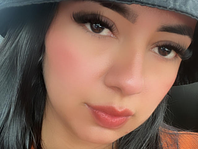 El rostro de KiraHolt, con un gorro gris, largas pestañas negras, rubor rosado y labios rojos, con una expresión ligeramente seria. Tiene ojos marrón oscuro y cabello negro..
