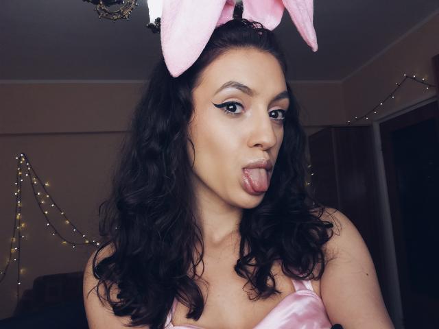 VievienneClemente with pink bunny ears, curly black hair, and pink lingerie, sticking her tongue out, showing off her eyeliner and full lips, with a cute, playful expression.