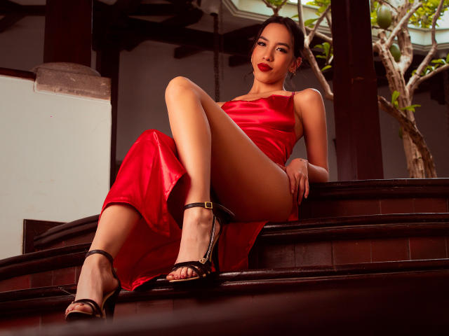 KylieWhite in a red satin dress, sitting on wooden stairs, legs spread, black high heels, red lipstick, confident smile, bare legs, dress revealing her pussy, dark brown hair.