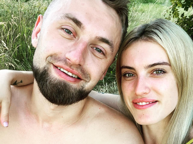 KrisAndVanessa, a shirtless dude with a beard and small tattoo on his shoulder, and Vanessa with blonde hair, smiling and standing outside. His hand rests on her shoulder.