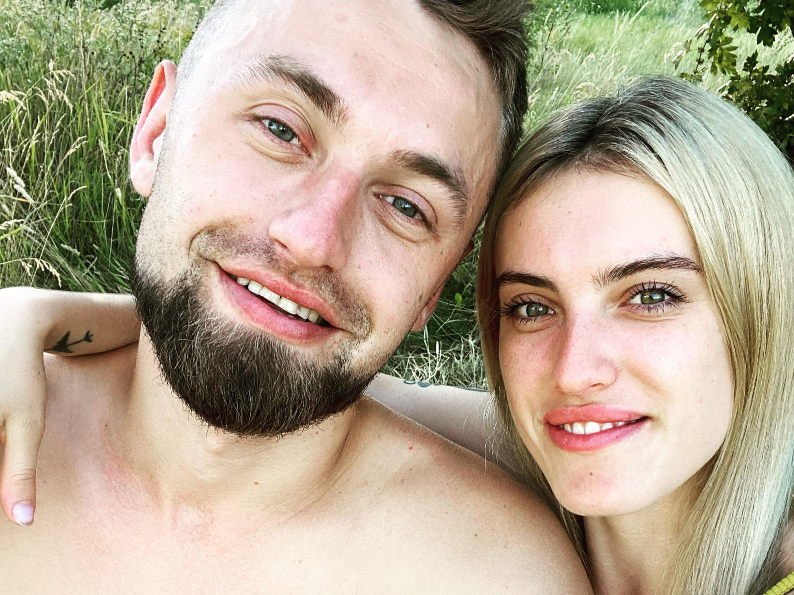 KrisAndVanessa, een man zonder shirt, met een baard en een kleine tatoeage op zijn schouder, en Vanessa met blond haar, die lacht en buiten staat. Zijn hand rust op haar schouder..