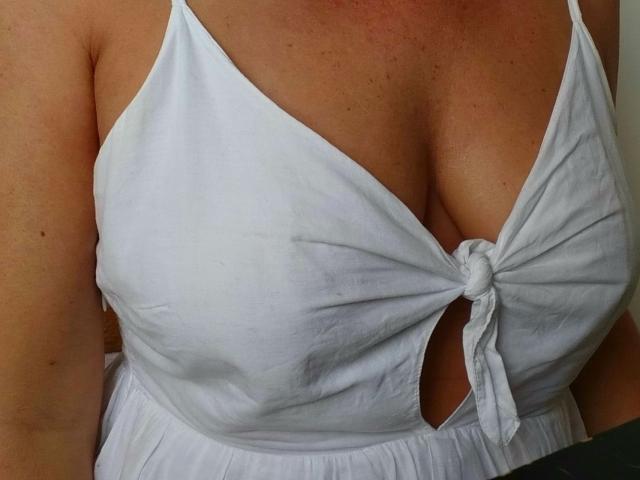 Das weiße, hochgeschlossene Kleid von MeahBrunette zeigt ihre großen, runden, weißen Brüste mit einem kleinen Ausschnitt. Ihre helle Haut hat feine Sommersprossen..