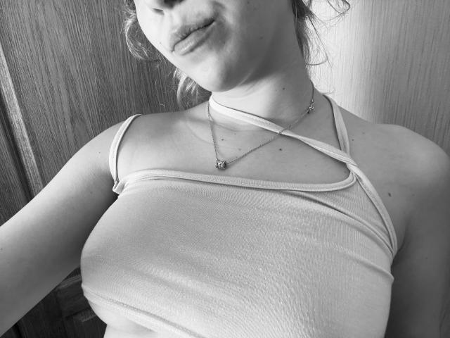 SugarrX with big tits, wearing a criss-cross halter top, showing her chest and neck, with a necklace, in a black-and-white photo. Her lips are slightly parted.