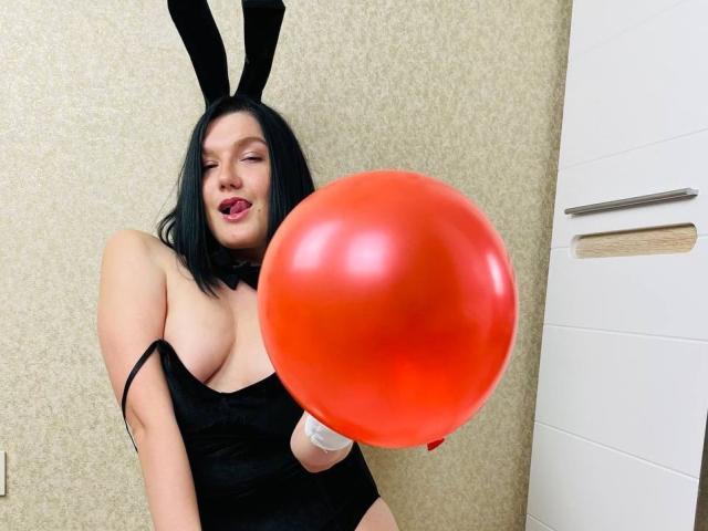 AngelinaLoveHot with black bunny ears, tongue out, holding a red balloon, wearing a black velvety one-piece that exposes her tits, white glove, and black bowtie.