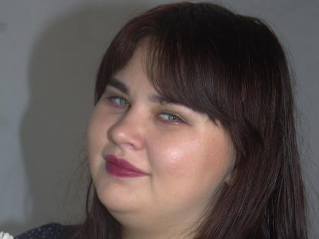 KaidoKun hat braunes Haar, grüne Augen und rosafarbenen Lippenstift mit einem leichten Lächeln. Ihre helle Haut ist leicht gerötet. Sie blickt leicht nach links..
