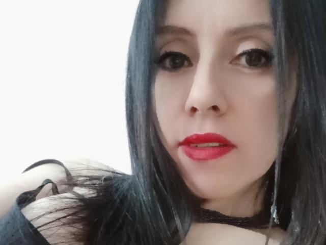 MondBlue has straight black hair, red lipstick, and dark eyes, looking slightly to the side with a subtle smile, wearing a black choker. Her pale skin contrasts with her red lips.