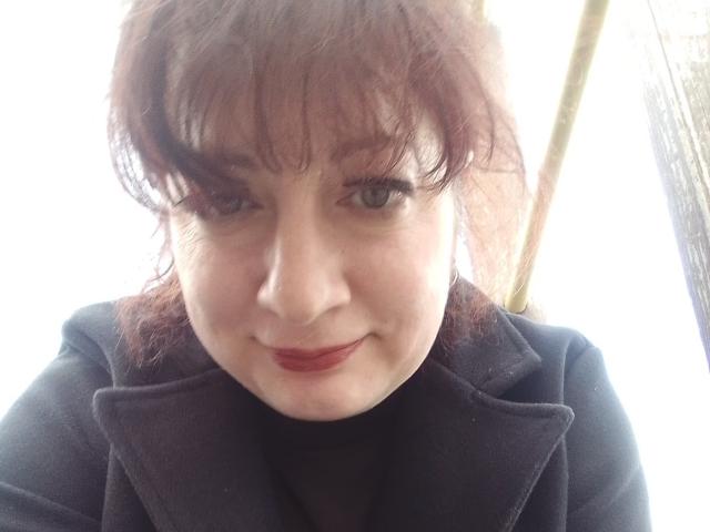 LediSusana ha la pelle chiara, i capelli castani con la frangia e il rossetto rosso. Indossa un cappotto nero, guarda in basso con un leggero sorriso e ha dei seni piccoli e discreti..