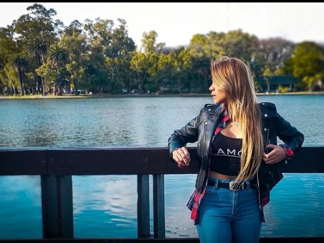 Stephaniez, con lunghi capelli biondi, indossa una giacca di pelle nera, una camicia a quadri rossa e jeans blu, ed è in piedi accanto a una ringhiera di legno, appoggiandovisi con le mani..