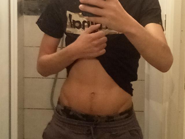 TeddyLeCoursier's toned belly, lifted black shirt, showing a flat stomach with a small belly button, wearing low grey pants, mirror selfie, hand holding phone, in a bathroom.