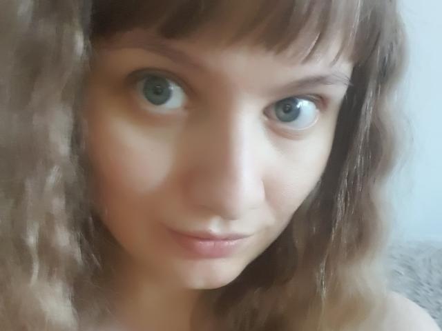 LinNatty has blue eyes, wavy brown hair with bangs, and a slight smile. Her skin is fair with a subtle blush. She's looking directly at the camera.