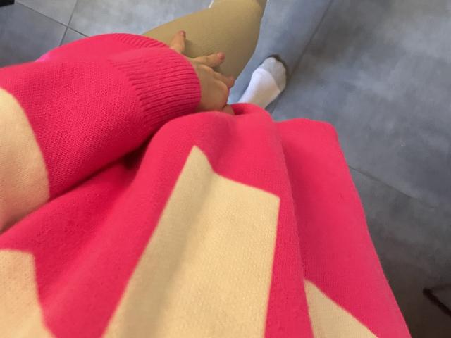 O suéter rosa com listras bege de RozalinaPleasure, as meias bege e a calça jeans azul, mostrando sua mão com esmalte vermelho descansando no joelho, fotografada de um ângulo ligeiramente superior..