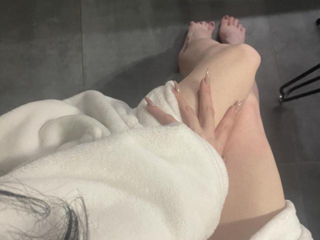 KatyKatt, con senos grandes, vistiendo un sujetador blanco de encaje y tanga a juego, sentada en una silla, sosteniendo su tanga, con un juguete sexual grande y rosa frente a ella..