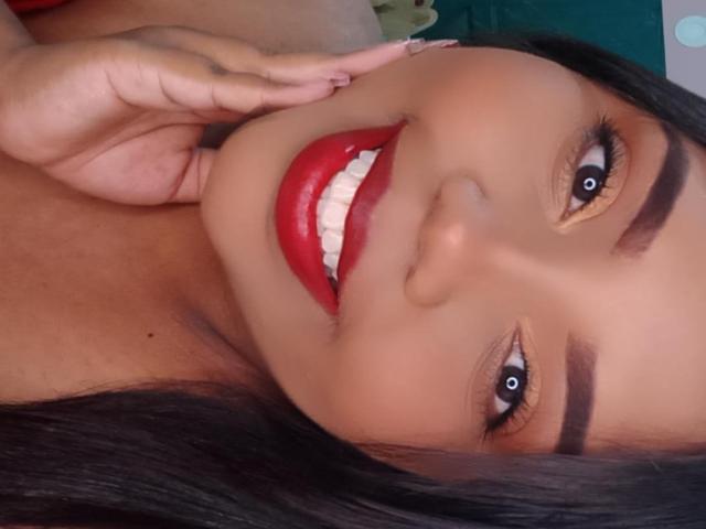 SarahSmity's face, dark brown skin, red lipstick, white teeth, brown eyes, black eyebrows, long black hair, hand touching cheek, smiling, wearing no clothes, cute, sexy.