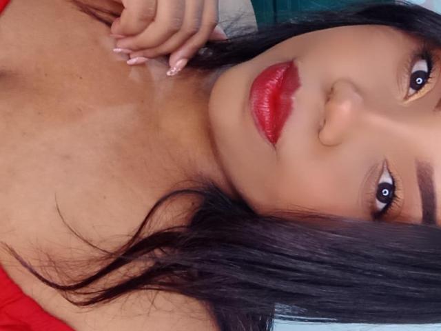 SarahSmity with red lips, black hair, and tan skin, looking up with a hand near her neck, showing her tits, and having a sexy, attractive face.