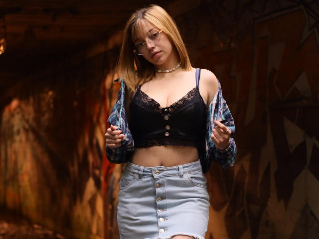 SophieMarkrov, com cabelo loiro, óculos, sutiã de renda preta, saia jeans abotoada e camisa xadrez, em pé, olhando para baixo, com as mãos na camisa, colar no pescoço, seios médios, atraente, em um ambiente urbano..