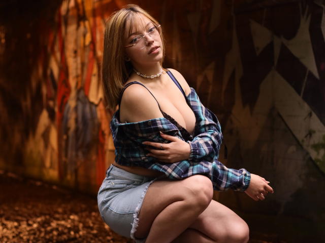 SophieMarkrov with glasses, plaid shirt off-shoulder, revealing big boobs, denim shorts, squatting, hand on chest, choker necklace, brown hair, slightly annoyed expression, graffiti wall background.