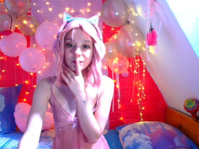 MissAstravert with pink hair, cat ears, and a pink lace nightie, shushing with her finger to her lips, surrounded by balloons and fairy lights. Her tits are small.