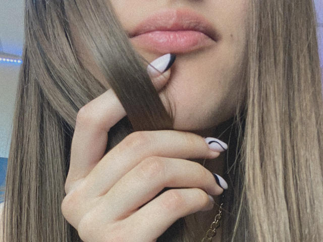Pingli's pink lips are slightly parted, with her long brown hair in front. She's touching her chin with a hand, nails painted white with black stripes.