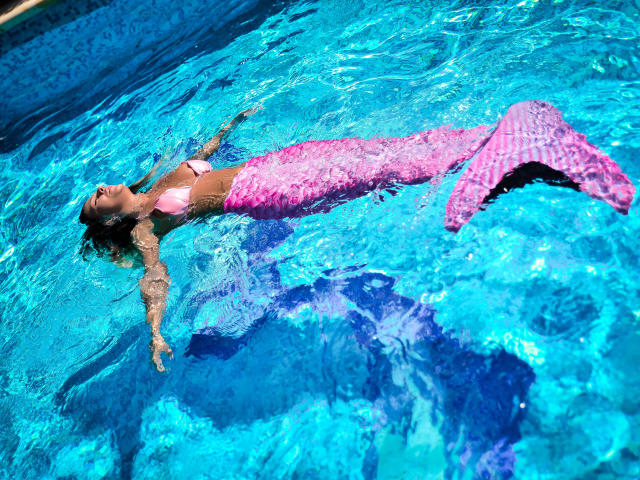 SpicyAlicia è una sirena rosa con una coda lucida, che galleggia in una piscina blu, con il sedere in alto, i seni sopra l'acqua, gli occhi chiusi e le braccia aperte..
