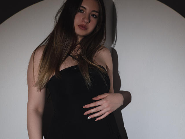 CleoLeo, con i suoi lunghi capelli castani, indossa un abito nero senza spalline, ha una mano sul ventre, guarda leggermente di lato, è in ombra, e mostra il seno e un trucco leggero..