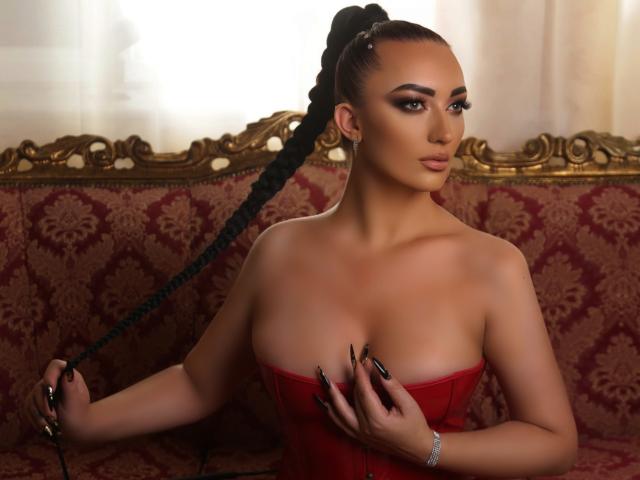 MiaBlackXO with a black braided ponytail, wearing a red strapless dress, holding a black ribbon, showing her tits, with manicured nails and a gold ring.