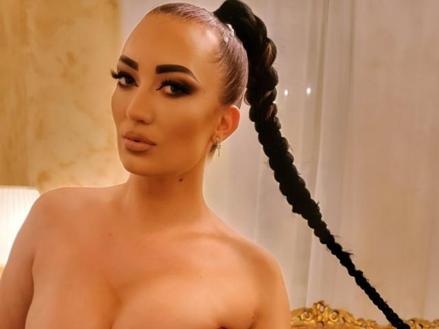 MiaBlackXO tiene una coleta alta con una larga trenza negra, cejas pobladas, delineador de ojos oscuro y lápiz labial nude, y aparece sin top, mostrando sus senos. Tiene una pequeña peca en el cuello..