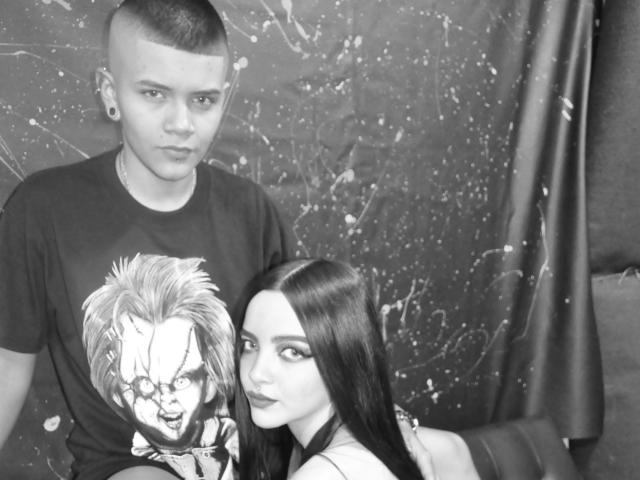 Photo en noir et blanc d'EmilyAndSam avec des cheveux courts et rasés, et des piercings aux oreilles, portant un t-shirt à motif, et d'EmilyAndSam avec de longs cheveux noirs, assise à côté de lui. Les seins d'EmilyAndSam sont visibles..