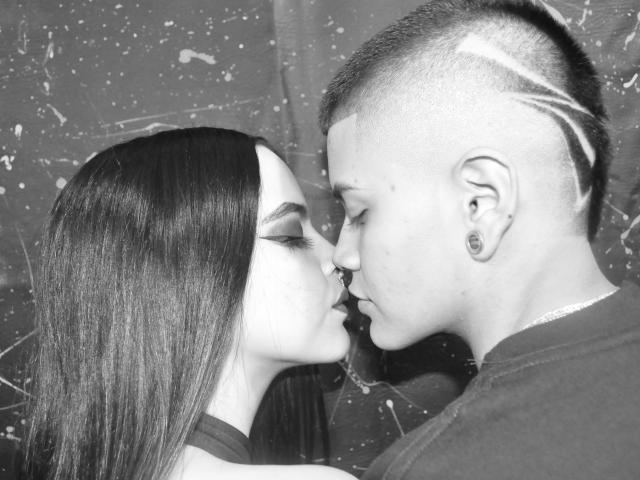 EmilyAndSam with long dark hair kissing Sam, who has a mohawk and ear gauges. EmilyAndSam's nose is touching Sam's nose. Black-and-white photo.
