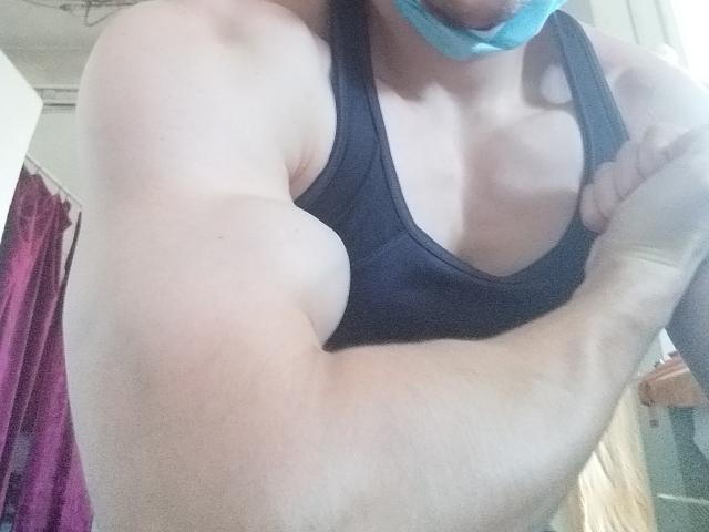 ConanJones with muscular arms, wearing a black tank top, and a blue face mask, showing defined biceps and a small chest. His skin is light, and his face is partially obscured.