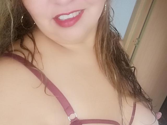 AmbarSimmons with wet brown hair, pink lips, and a maroon bra showing her tits. Her skin is light, and she's smiling slightly. A door is in the background.