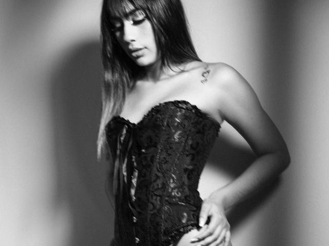 Jessica Soler, con lunghi capelli scuri, indossa un corpetto di pizzo nero, una mano appoggiata sul fianco, occhi chiusi, tatuaggio sulla spalla destra, ombra delicata, fotografia in bianco e nero..