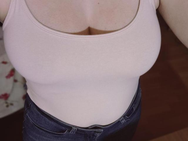 Les seins de SpicyGrace, vus dans un débardeur rose qui dévoile sa poitrine, associés à un jean bleu et une ceinture blanche visible. Sa peau est claire et sa poitrine est proéminente..
