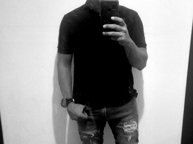 Matteo's zwarte shirt en versleten jeans, zijn gespierde armen en een horloge, terwijl hij een telefoon vasthoudt om een spiegel-selfie te maken, zijn gezicht is afgesneden, op een zwart-wit foto..