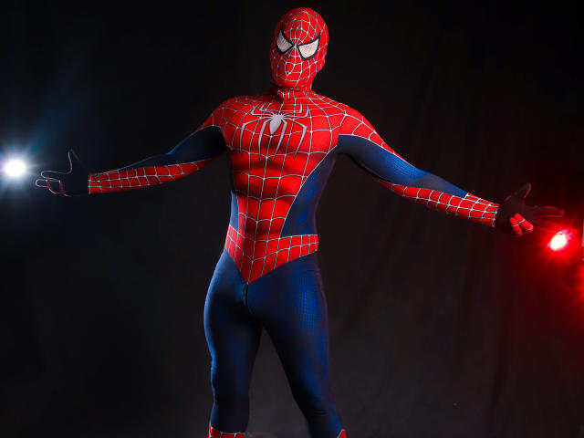 SebastiianMaxime in a red and blue Spider-Man suit with web patterns, standing with arms out, glowing red and blue lights on each side, wearing a mask.